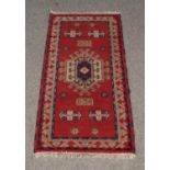 A small red ground rug with an Aztec design. Length: 120cm, W: 64cm. Condition good. No holes.