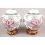 A pair of large cloisonné ginger jars decorated with flowers. On oriental carved wooden stands.