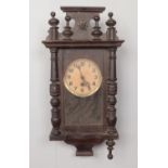 A wooden cased wall clock with pendulum, with carved wooden plinth and finial decoration. Comes with