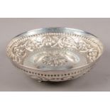 A silver bowl with repousse decoration and central floral design. Raised on three supports.