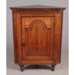 A Georgian oak and mahogany corner cupboard. With later supports. Split to door.
