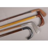 Two walking sticks along with two wooden shaft golf clubs. One stick with bird of prey handle.