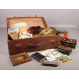 A vintage suitcase with collectables. Vintage postcards, various framed oil on canvas, advertising