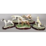 Four ceramic figures of racing dogs on wooden plinths.