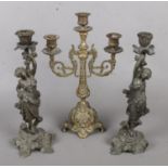 A Pair of Cast Metal Decorative Figural Candlesticks, together with another Brass Example. Some