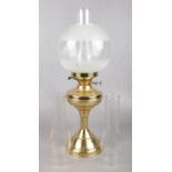 A brass based oil lamp with etched glass shade and spare chimneys.