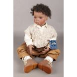A Porcelain Celia Sitting Doll, 'Taylor' 9/200, in Beige Clothing and Suede Boots.
