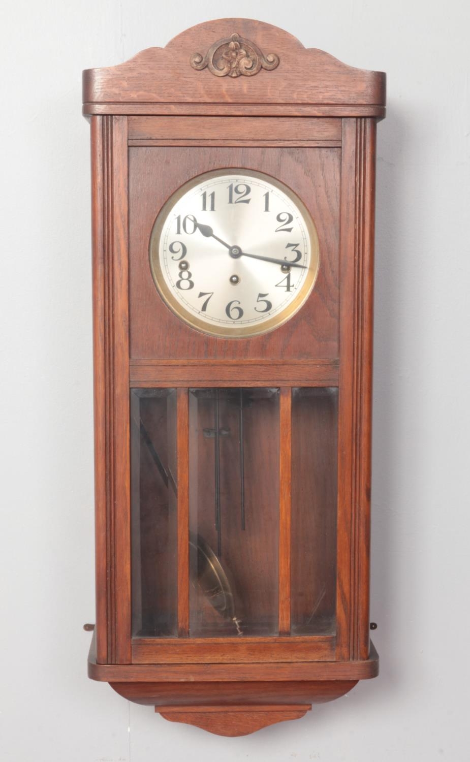 A 1930's wall clock with eight day striking movement, bevelled glazed oak case, pendulum and key.