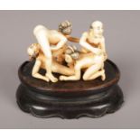 A Japanese carved ivory erotic okimono on wooden stand. Okimono 5cm x 8cm x 4.5cm.