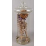 A large glass decanter with spigot to the bottom, containing a dried thistle.