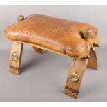 A vintage camel saddle stool with worked leather seat and brass mounts.