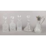 Four cut glass decanters along with a Falstaff claret jug. One decanter has a broken stopper.