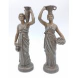 Two ornamental figurines of Greco/Roman women carrying pots, standing approx 18cm tall.