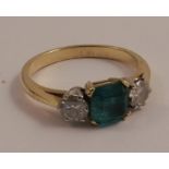 An emerald and diamond three stone ring, unmarked, the square step cut stone flanked either side