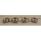 A set of four silver open salts, with engraved floral decoration, raised on three scroll supports