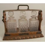 An oak and gilt metal three bottle tantalus, fitted with three square cut glass decanters, height