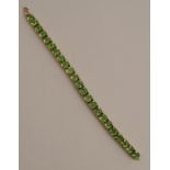 A peridot 9 carat gold bracelet, set with twenty three cushion shaped stones, 19cm long, 23g gross