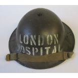 A WW2 drab coloured metal helmet, stencilled with "LONDON HOSPITAL" in white to one end