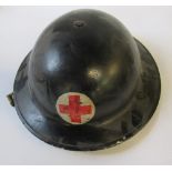 A WW2 metal helmet, painted black with a Red Cross emblem to each end, rim stamped "74"