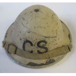 A WW2 metal helmet, painted cream, with the letters "C.S."  printed one end