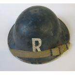 A WW2 metal helmet, painted blue with "R" in white to one end, indistinctly impressed to the rim