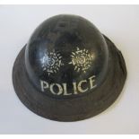 A WW2 metal helmet, painted black with POLICE and two crests in white to one end, the rim covered