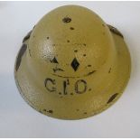 A WW2 metal helmet, painted beige with the letters "G.I.O." in black to the ends