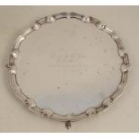 A circular silver salver, with shaped edge, having a presentation inscription, raised on three