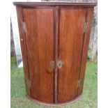 An antique oak corner cupboard, with mahogany banding, the barrel front opening to reveal shelves,