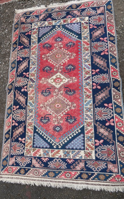 An Eastern style rug, having red medallions, and three lozenge motifs to a blue border, 80ins x