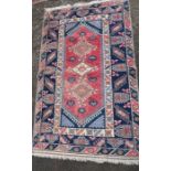 An Eastern style rug, having red medallions, and three lozenge motifs to a blue border, 80ins x