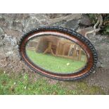 An oval mahogany framed mirror, with carved ebonised decoration and bevelled plate, max width 32.