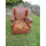 A leather wing back fireside chair, in distressed condition