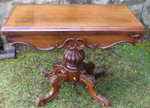 A 19th century fold over games table, raised on a turned and carved column, with four carved