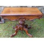 A 19th century fold over games table, raised on a turned and carved column, with four carved