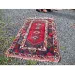 An Eastern design rug, decorated with four central medallions to a red field and patterned border,