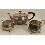An Arts and Crafts style silver three piece tea set, with hammered finish and raised on scroll legs,