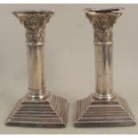 A pair of silver table candlesticks, formed as columns with Corinthian capitals and stepped square