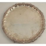 A silver salver, with gadrooned and shell shaped edge, raised on four ball and claw feet,