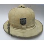 A WW2 German Afrika Korps style pith helmet, with chin strap and insignia to each side, having red