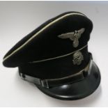 A WW2 style German SS visor cap, in black with white piping, bearing metal SS eagle and skull badges