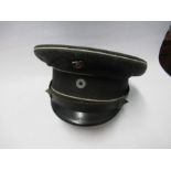 A Third Reich style visor cap, in dark grey wool, with white piping, and black leather effect chin