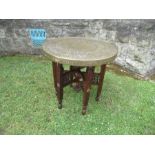 A brass Benares topped table, the wooden folding base with carved and inlaid decoration, diameter