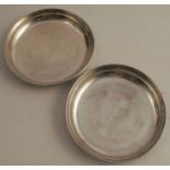 Two white metal circular dishes, one engraved with a crest, both with inscriptions to the underside,
