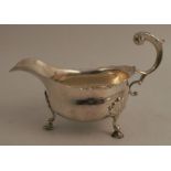 A silver sauceboat, with scroll handle, shaped edge and raised on three hoof feet, London 1909,