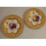 A pair of Royal Worcester plates, decorated with central panels of fruit to a yellow and git border,