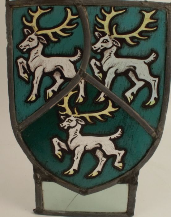 An Antique stained glass panel, of shield form, decorated with three stags, rectangular panel below,