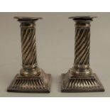 A pair of silver candlesticks, with wrythern fluting to the columns, raised on square bases with