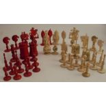 A collection of carved bone chess pieces, some carved with puzzle balls, natural or stained red,