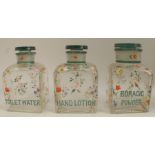 A set of three square glass bottles, with stoppers, decorated with flowers and inscribed Toilet